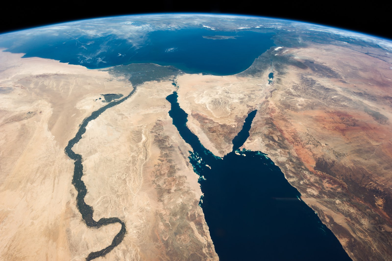 Color photograph taken from orbit: the green ribbon of the Nile and its delta on the left, the triangle of the Sinai Peninsula between the Gulf of Suez and the Gulf of Aqaba in the center, the coast of the Levant and the Dead Sea beyond it, the deep blue Mediterranean above and the curve of the Earth along the top.