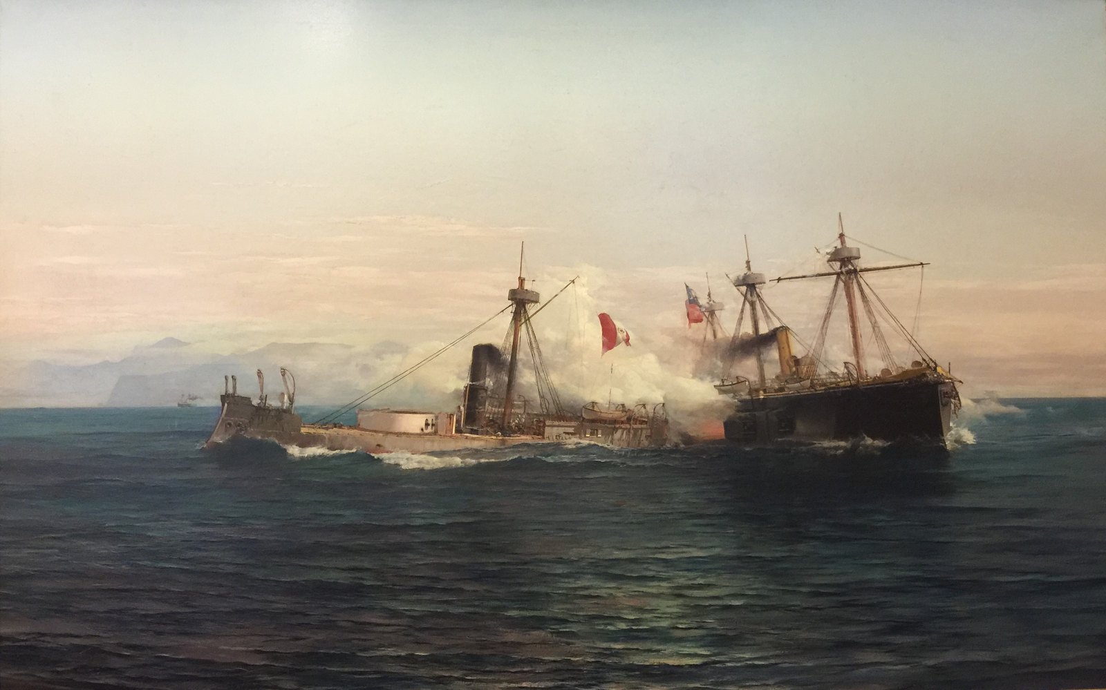Painting of a naval battle at sea under a pale sky: a low, battered Peruvian monitor with a red and white flag in the center, wreathed in gunsmoke, and a larger black Chilean ironclad with masts and a flag firing at close range on the right, with mountains along the coast behind.