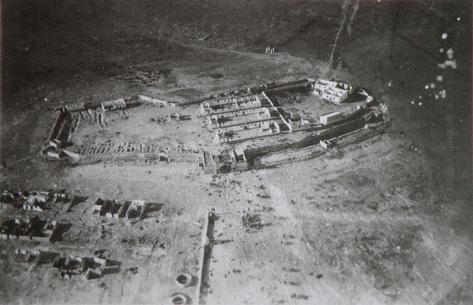Grainy black and white aerial photograph of a ruined desert fort with walls and roofless buildings, surrounded by bare ground, taken in October 1921.