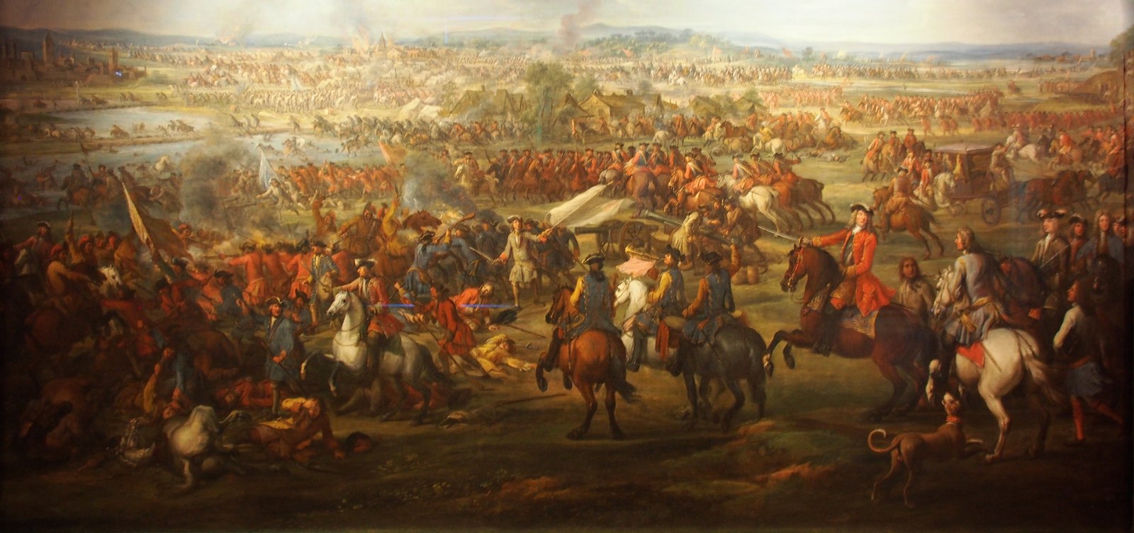Painting of a wide battlefield with masses of cavalry in red and blue coats charging across open fields, officers on horseback in the foreground and smoke over villages in the distance.