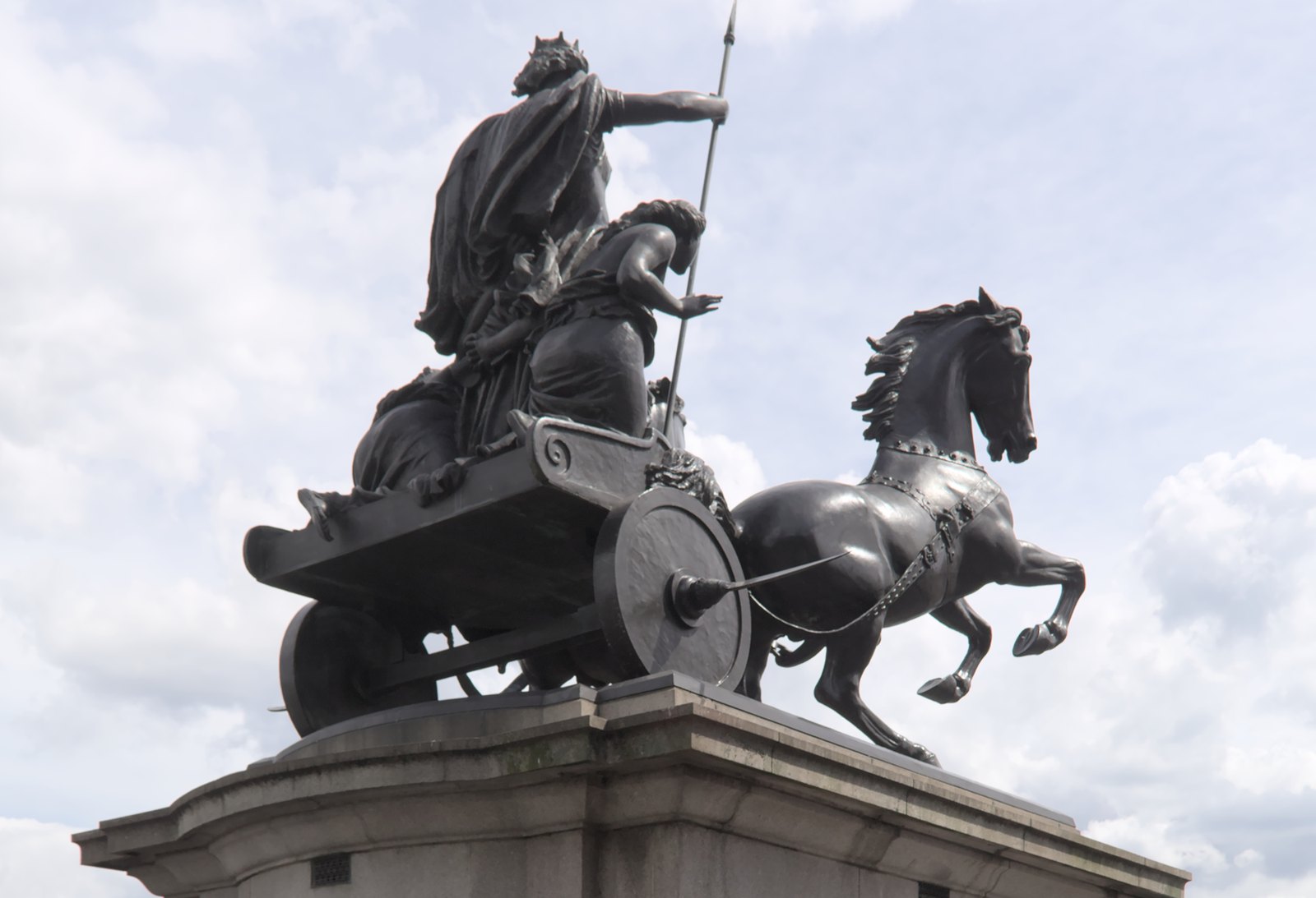 Bronze statue of Boudica standing in a chariot with a raised spear, her daughters crouching beside her and two rearing horses in front, Thomas Thornycroft's group by Westminster Bridge in London, set up in 1902.