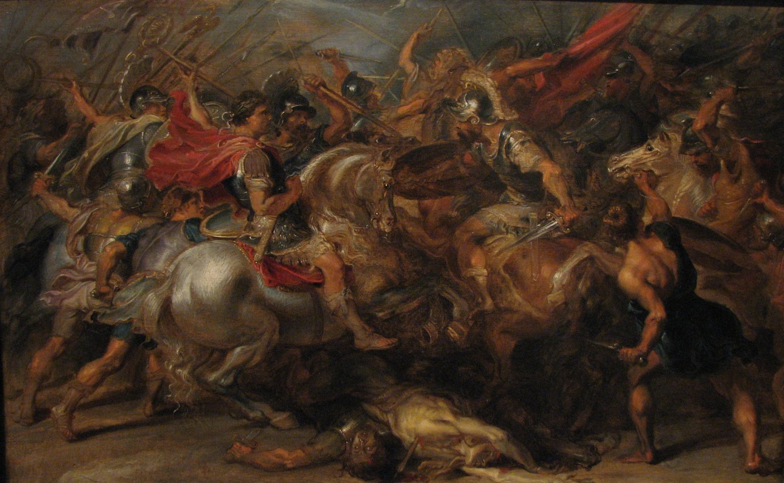 Baroque painting of a fierce cavalry melee: a rider in a red cloak on a gray horse at the center, armored horsemen clashing with swords under raised spears and banners, and a fallen soldier lying beneath the horses.