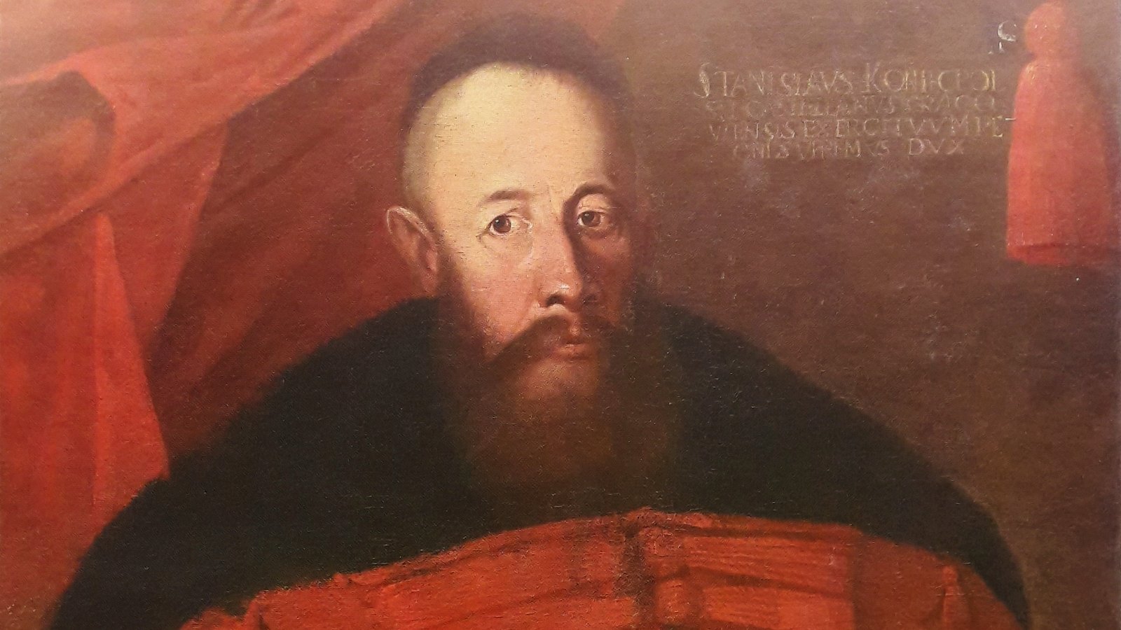 Portrait of Hetman Stanisław Koniecpolski: a heavily built man with a shaved head and a long brown beard, in a red żupan with many buttons and a dark fur collar, before a red curtain.