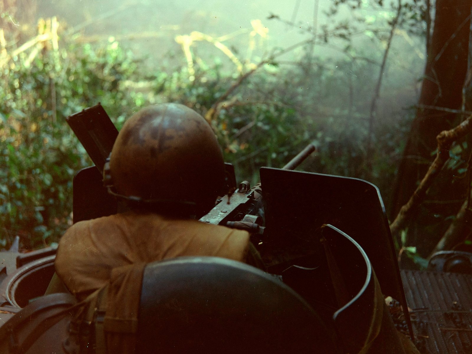 Black and white photograph of an American platoon sergeant, seen from behind, firing a .50 caliber machine gun mounted on top of an M113 armored personnel carrier during Operation Junction City in 1967.