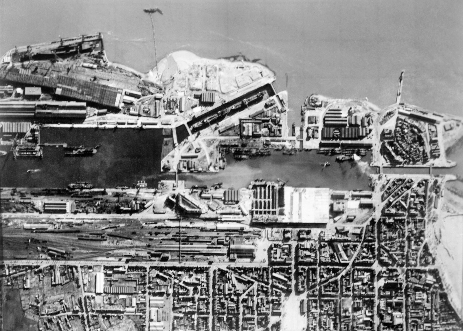 Black-and-white aerial photograph of the port of St Nazaire in 1942, showing the long Normandie dry dock, the harbor basins and the grid of the town beside the Loire.