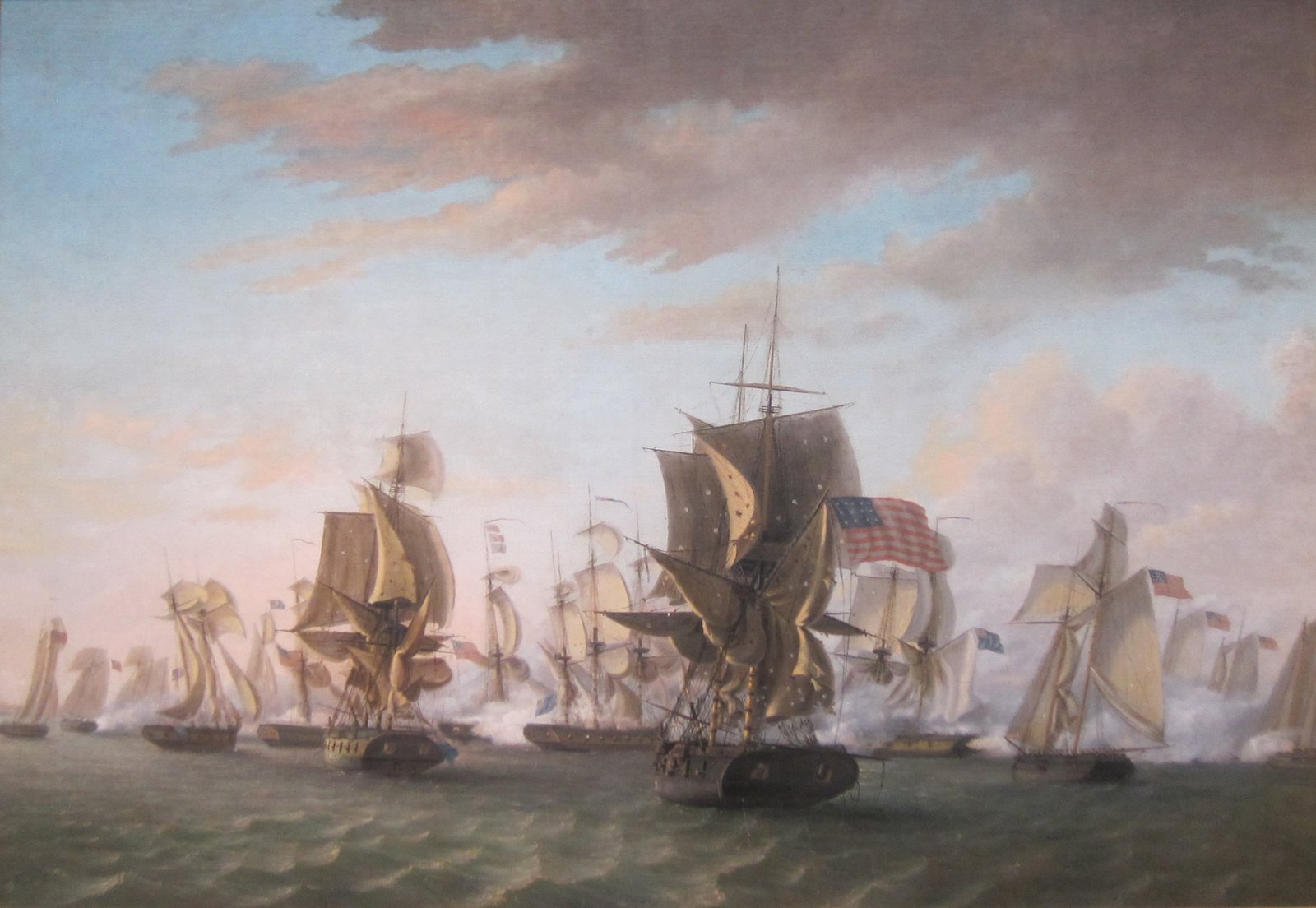 Oil painting of a naval battle on a choppy lake: a brig flying a large American flag sails into the center of a line of British and American warships wreathed in gun smoke, under a broad sky of pink and gray clouds.