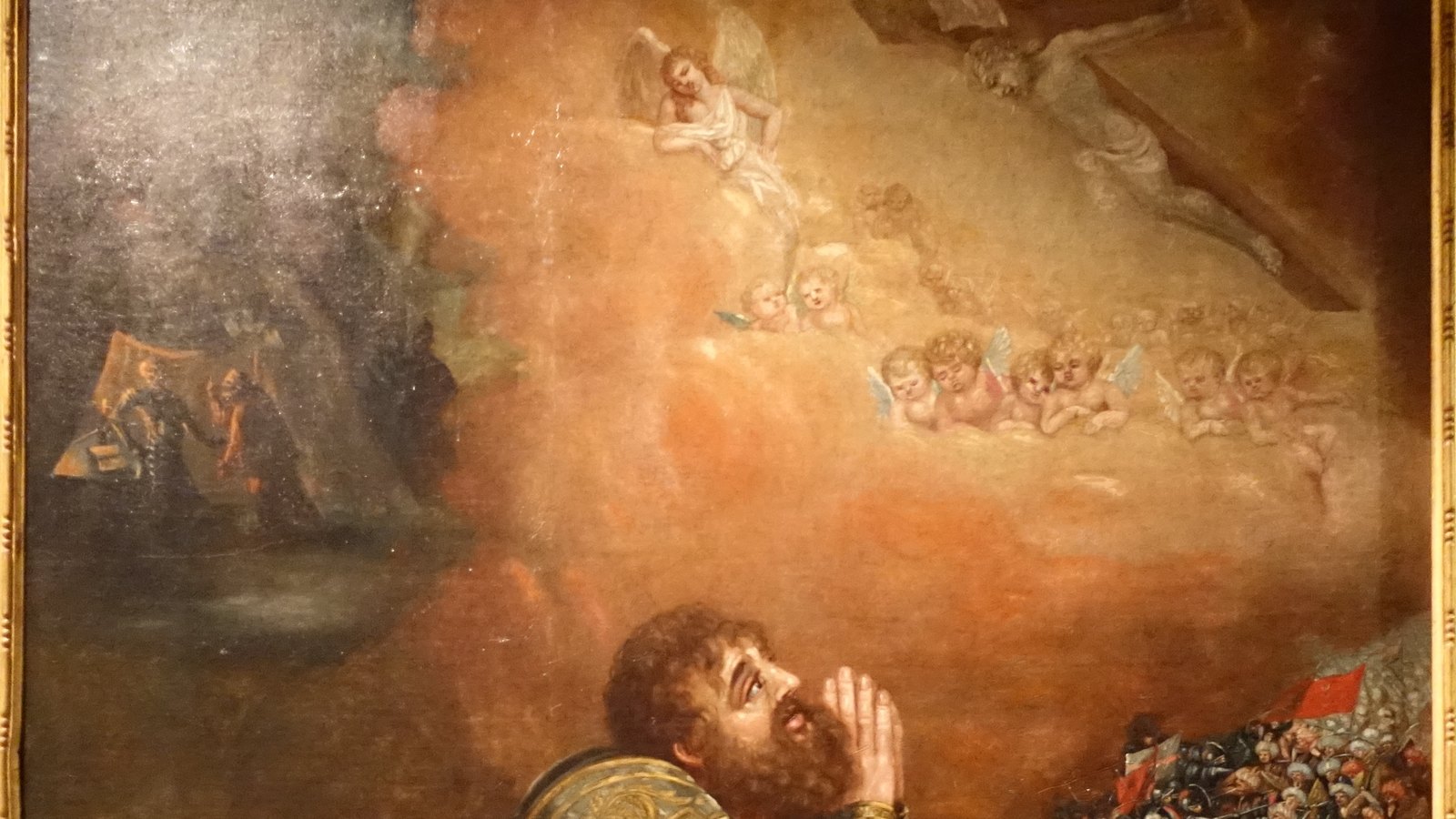 Seventeenth-century painting of a bearded knight in gilded armor kneeling in prayer, looking up at Christ on the cross among angels, with a cavalry battle on the right.