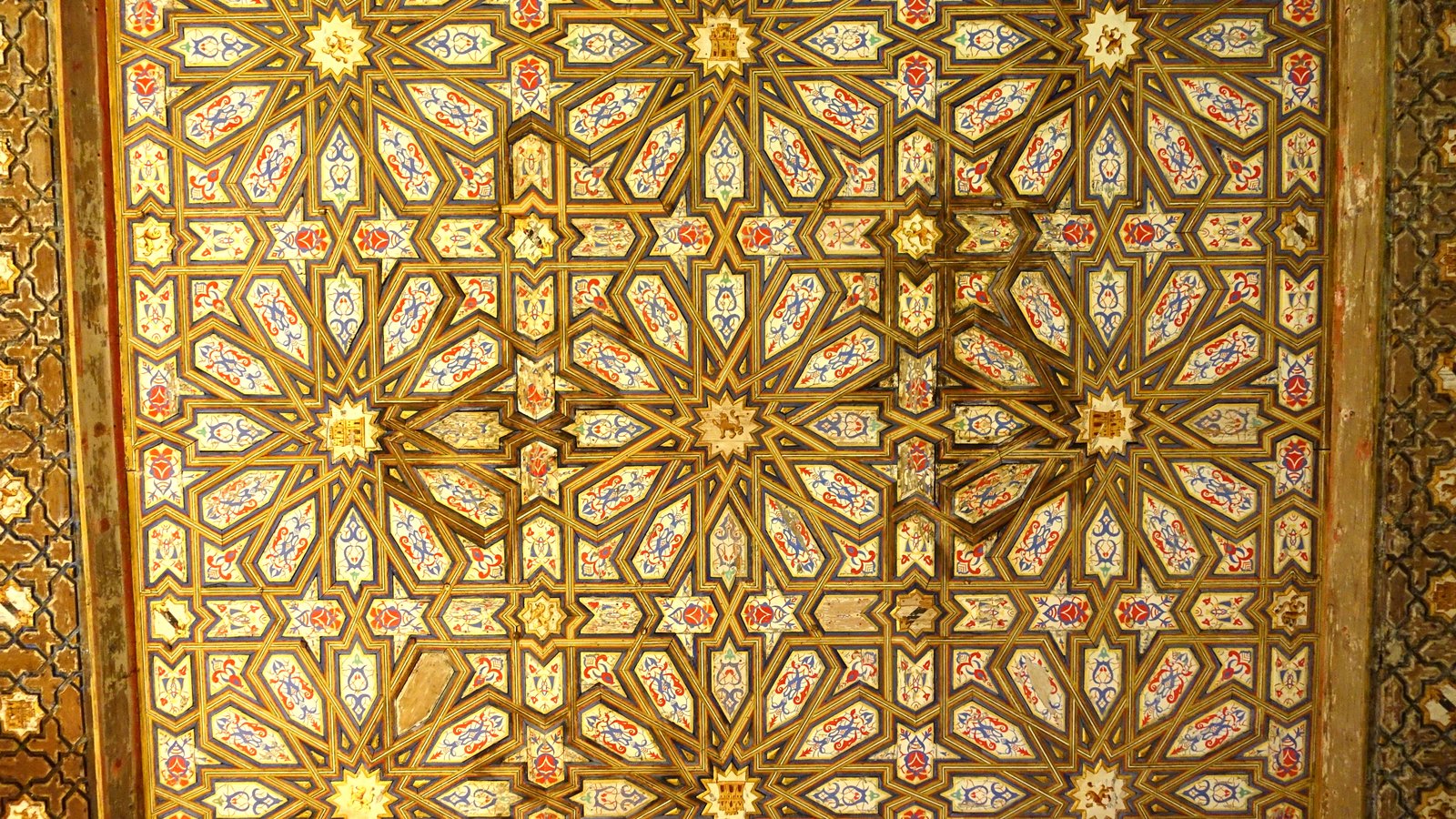 Painted and gilded wooden ceiling with interlacing star patterns in red, blue and gold.