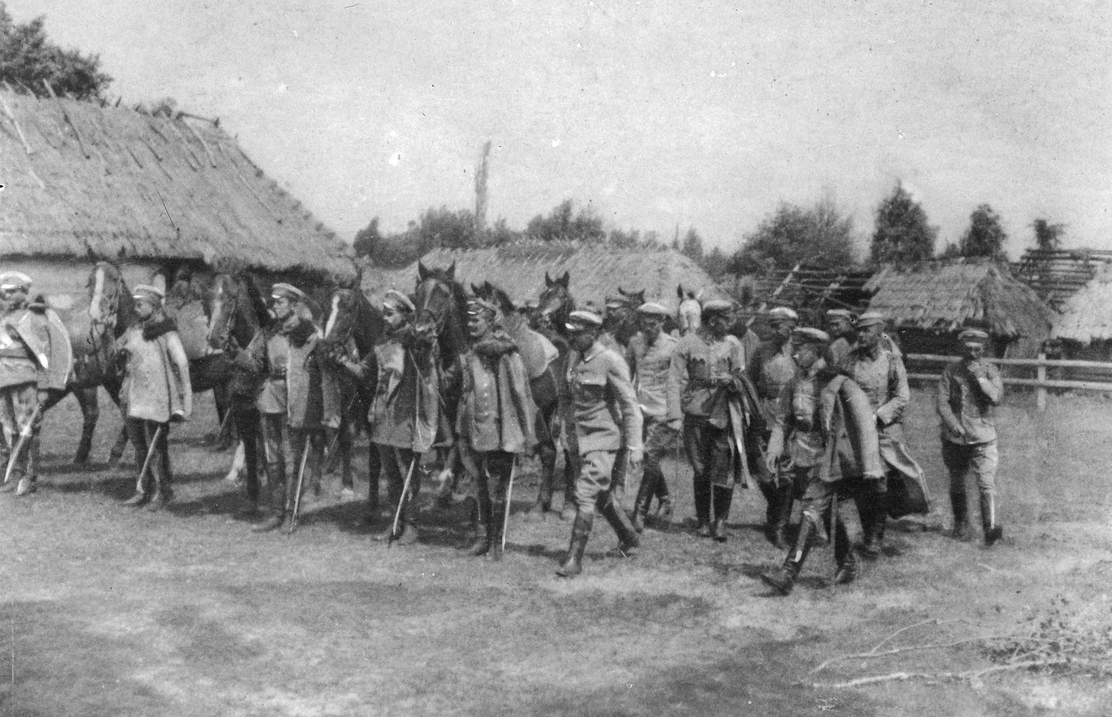 Black and white photograph of Józef Piłsudski at the head of a group of Polish Legion soldiers, some leading horses, walking past thatched cottages in a village