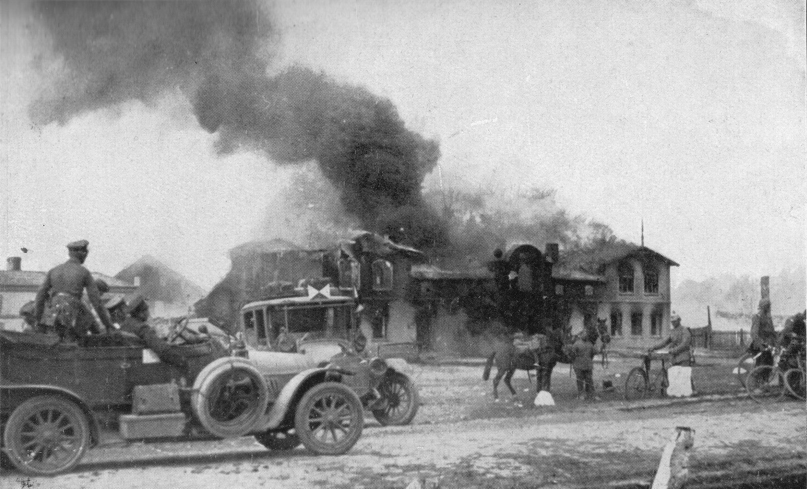 Fotografia płonącej gospody w Uzdowie 27 sierpnia 1914 roku z niemieckim samochodem sztabowym i żołnierzami na pierwszym planie