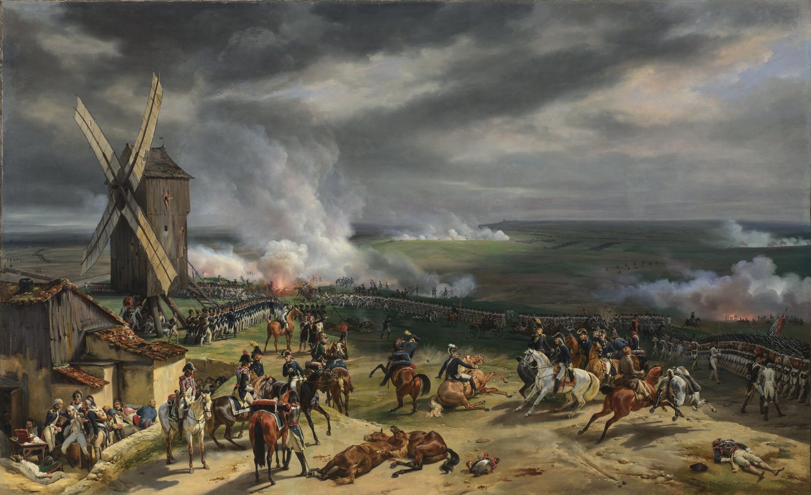 Painting of a windmill on a hill under heavy gray clouds, with white gunsmoke drifting over long lines of French infantry, mounted officers and fallen horses in the foreground, and wounded men by a farmhouse on the left.