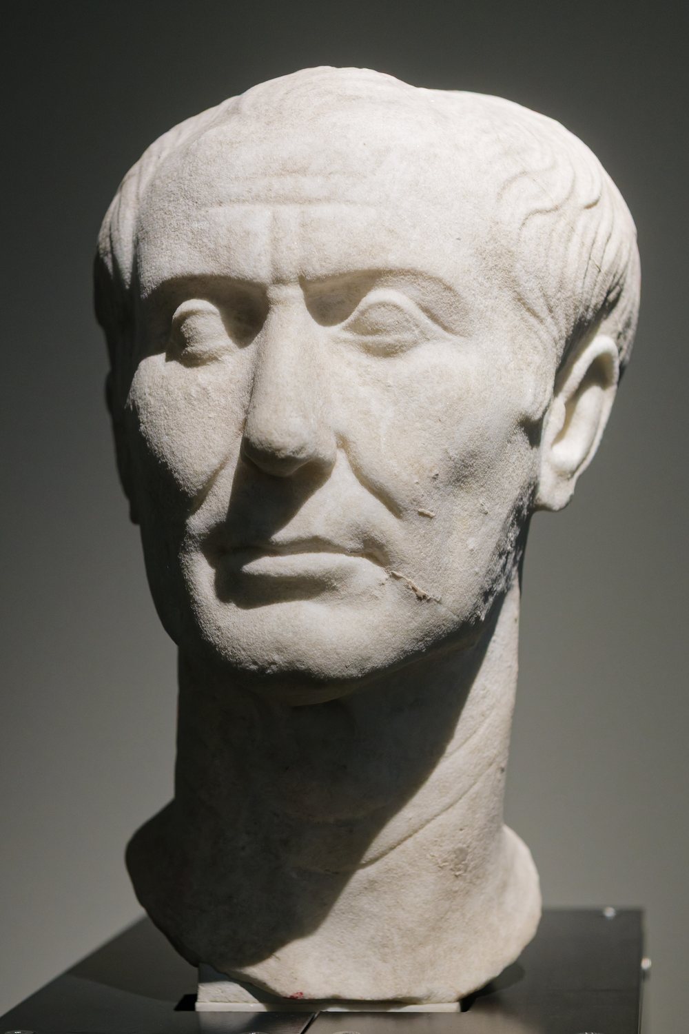 Weathered marble portrait head of Julius Caesar with a lined face and receding hair