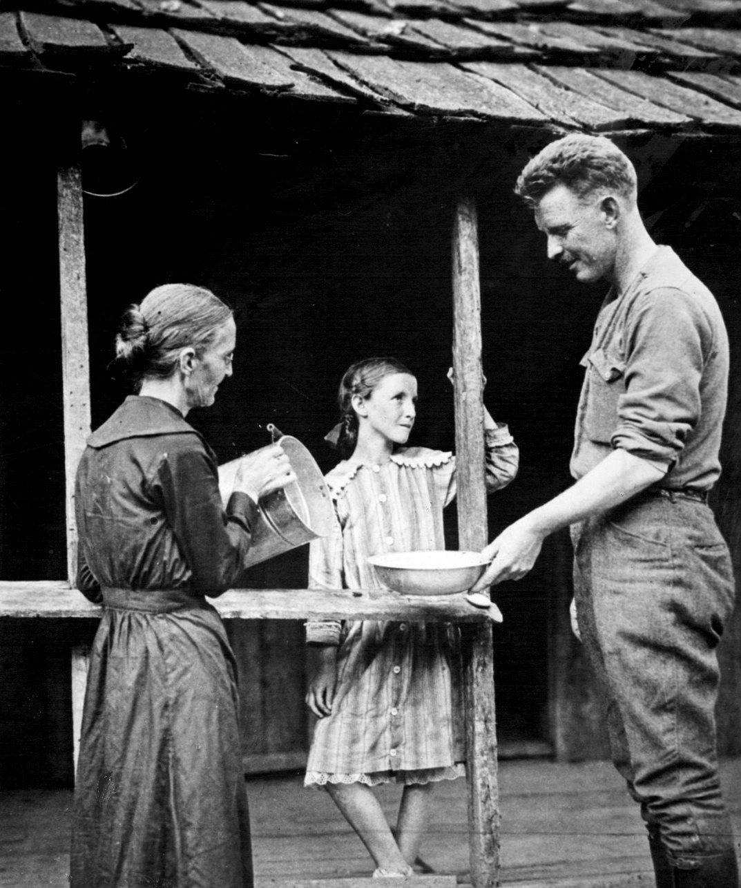 Photograph of Alvin York in uniform washing at a basin on a cabin porch while his mother pours water
