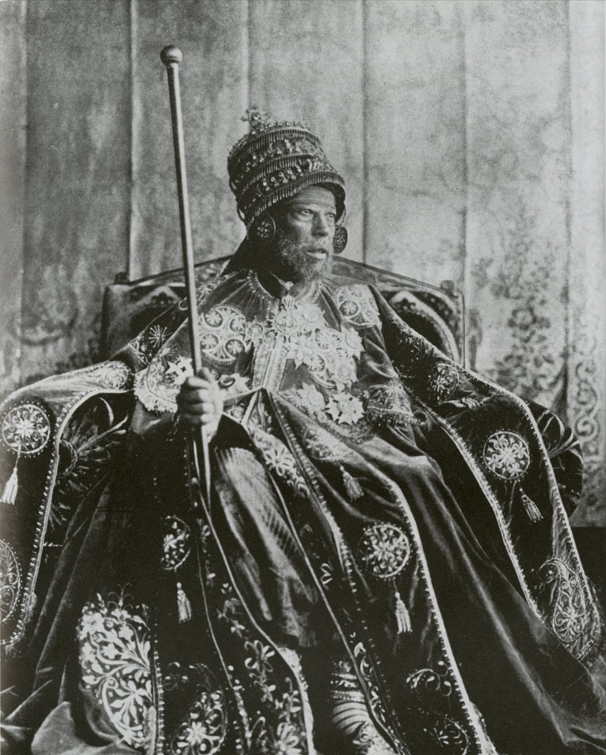 Black and white photograph of an Ethiopian emperor in a crown and embroidered robes on a throne