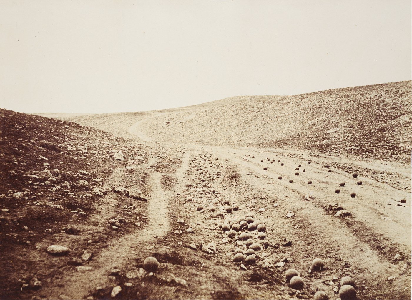 Sepia photograph of a barren road through a valley littered with cannonballs