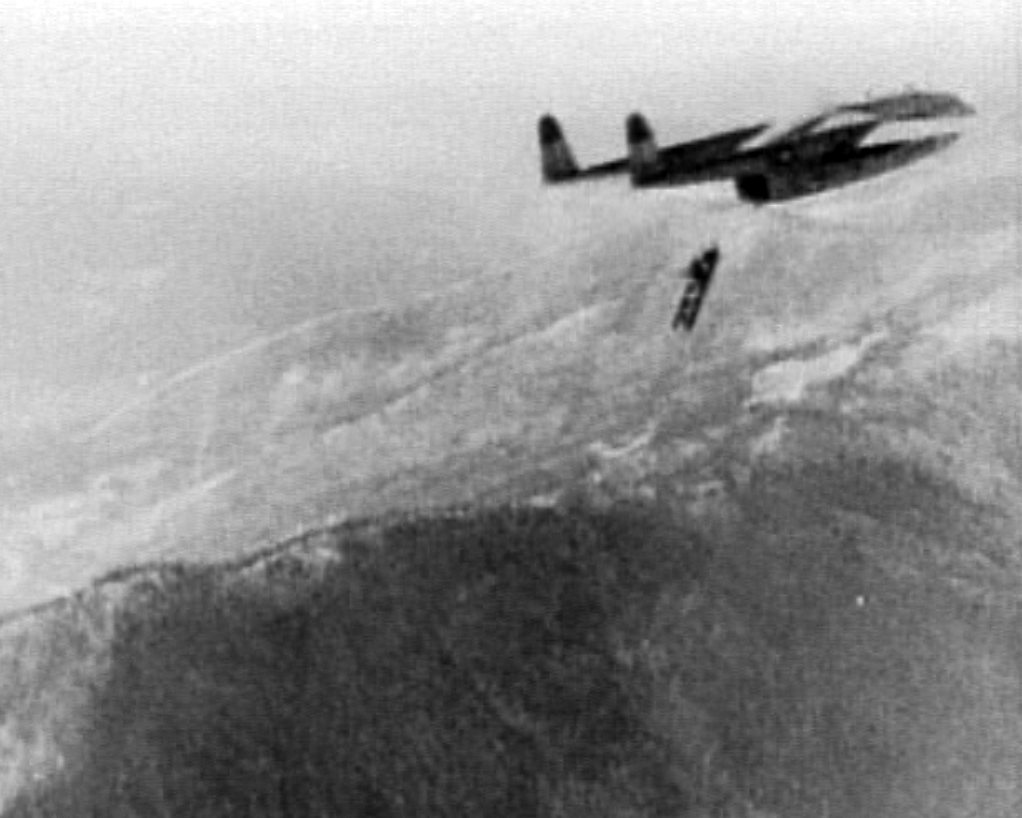 Photograph of a large steel bridge section falling from the open rear of a transport aircraft