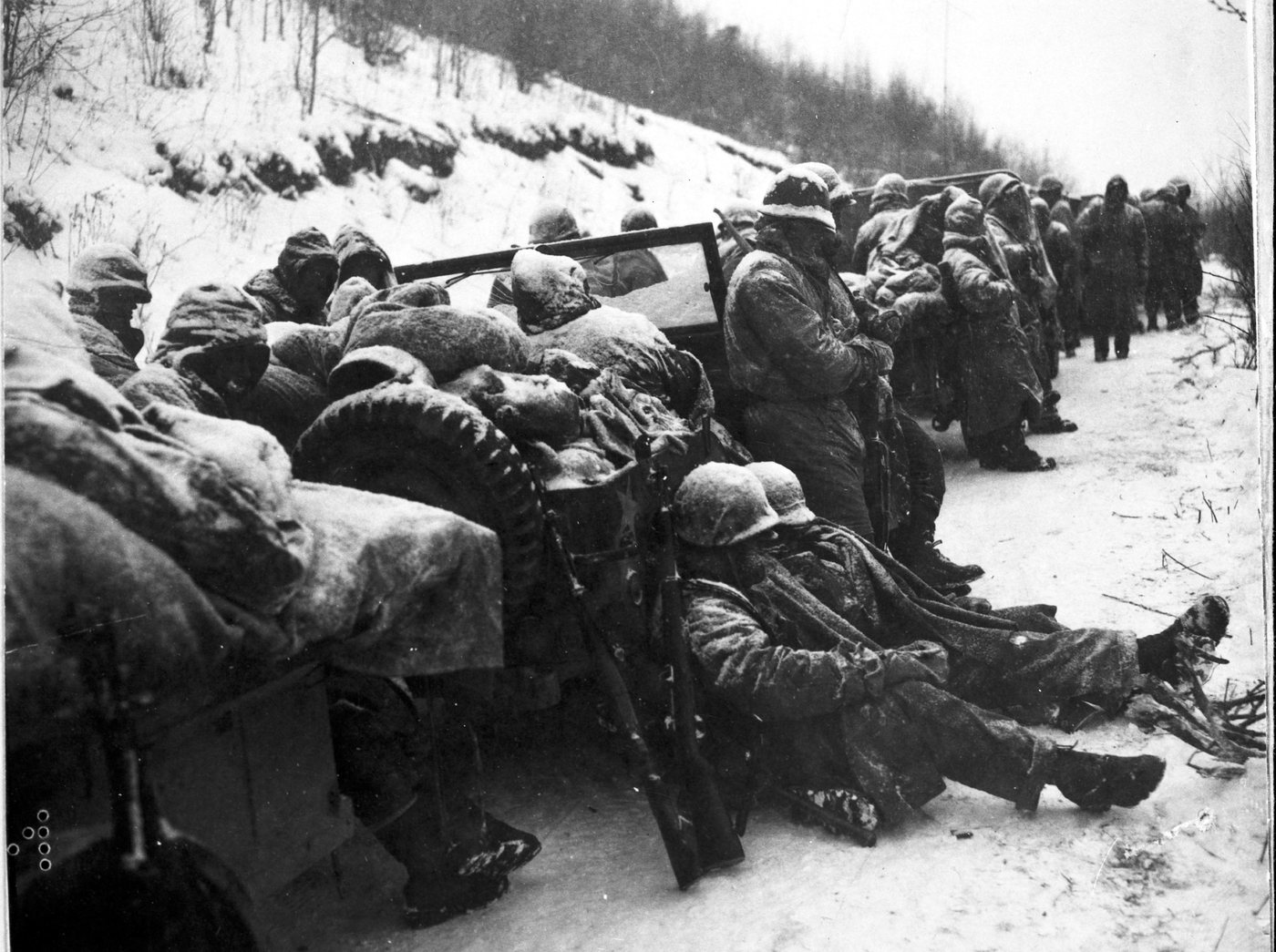 Black and white photograph of Marines huddled in the snow against parked vehicles