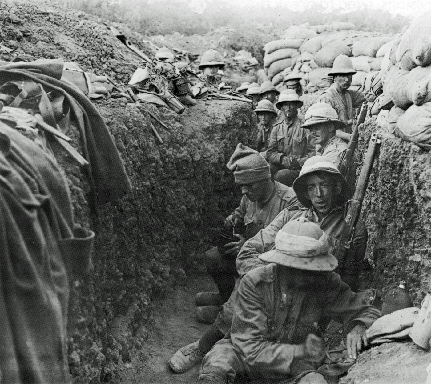Photograph of soldiers in sun helmets crowded into a narrow sandbagged trench