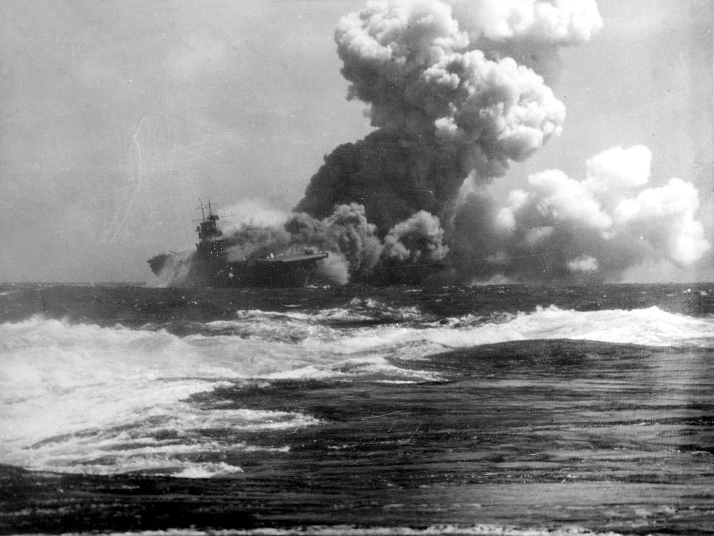 Photograph of an aircraft carrier pouring thick smoke at sea