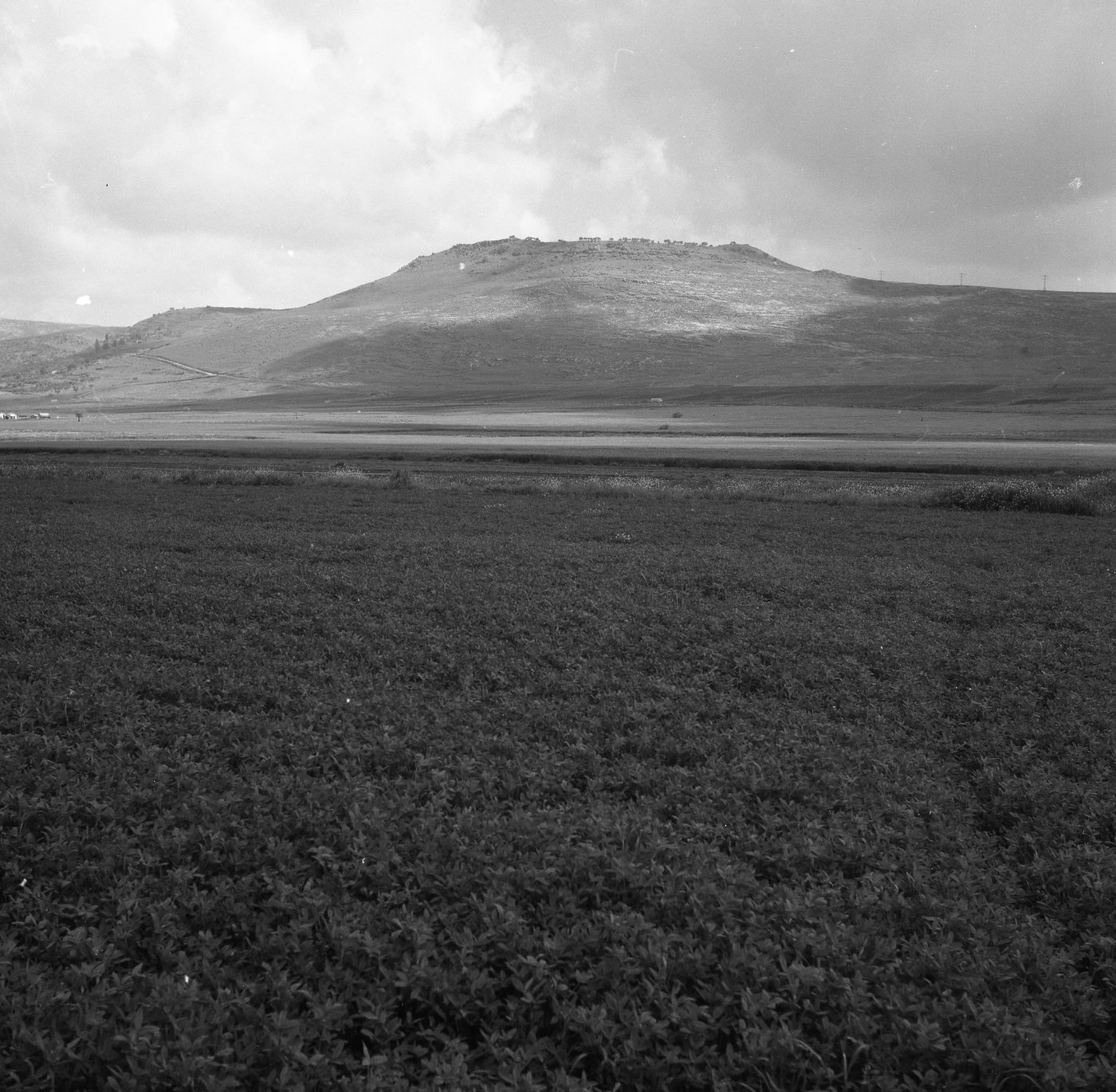 Black and white photograph of a low flat-topped hill rising above open fields