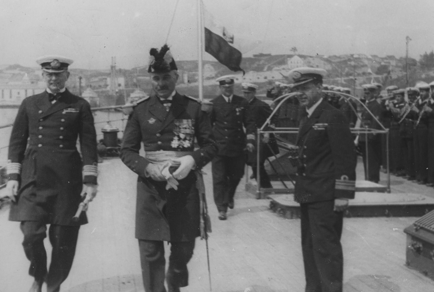 Photograph of naval officers in dress uniform walking on the deck of a ship