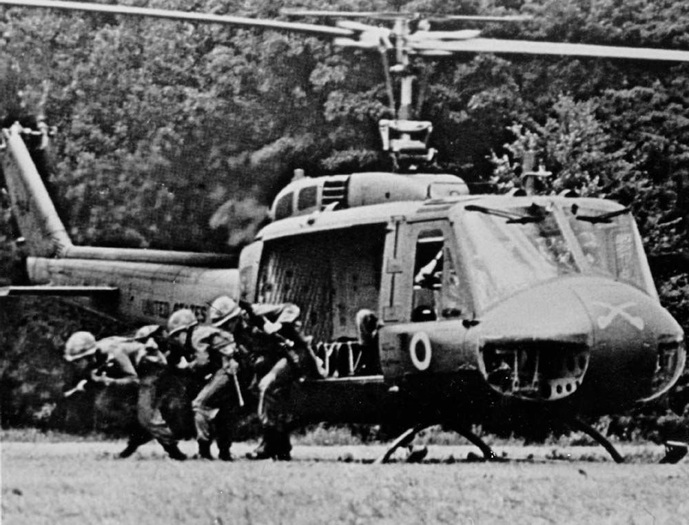 Photograph of infantrymen running from a Huey helicopter that has landed in a field