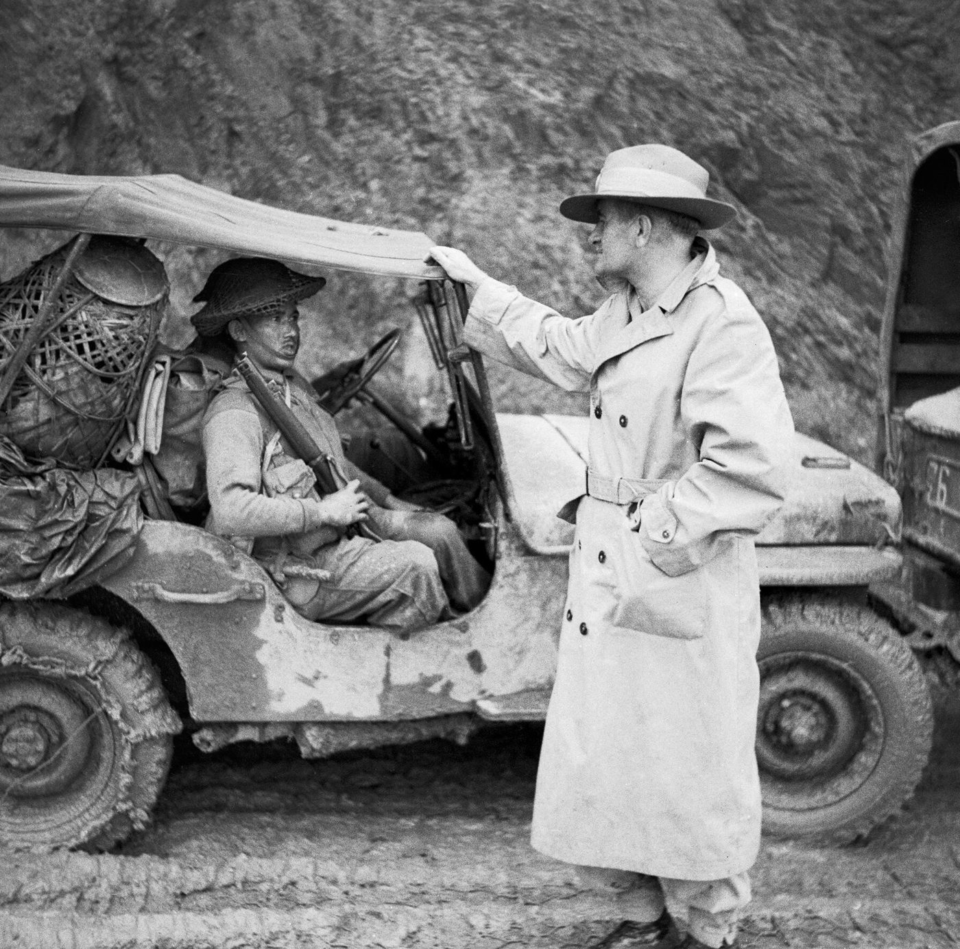 British general in a slouch hat talking with a smiling Gurkha soldier beside a jeep