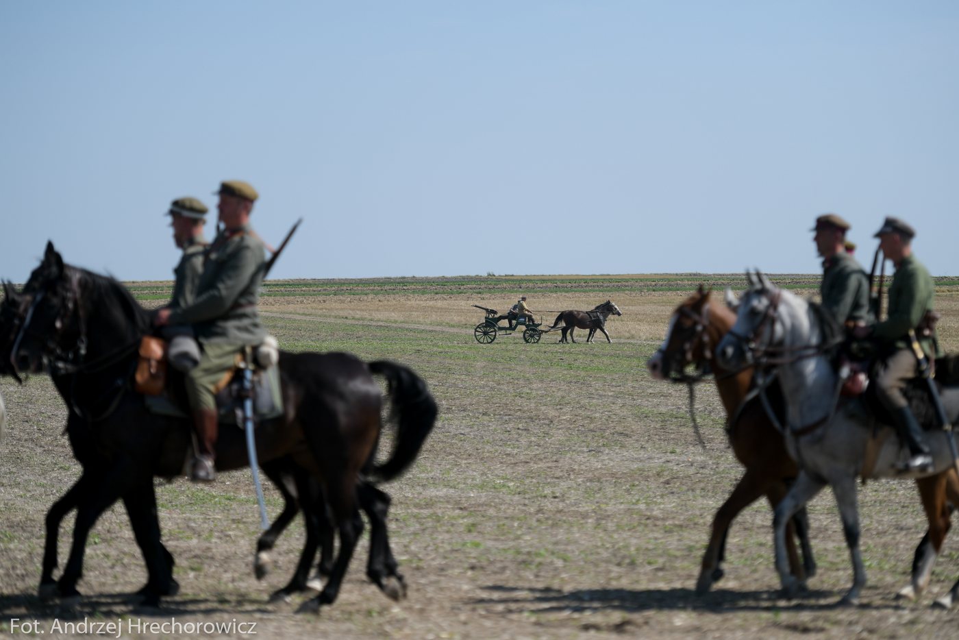 Konni rekonstruktorzy w mundurach khaki jadą przez otwarte pole
