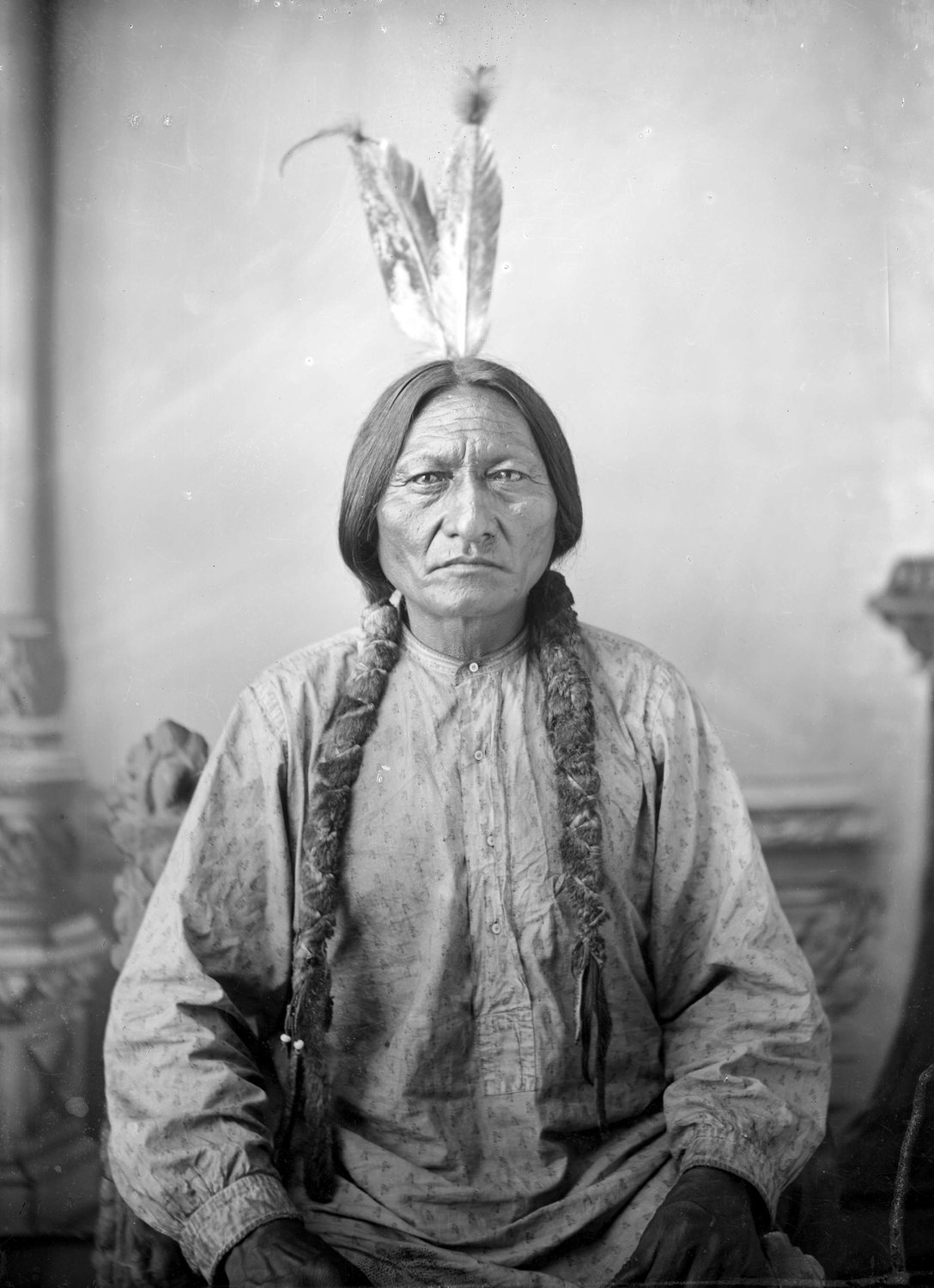 Black and white studio portrait of Sitting Bull with feathers in his hair and braids