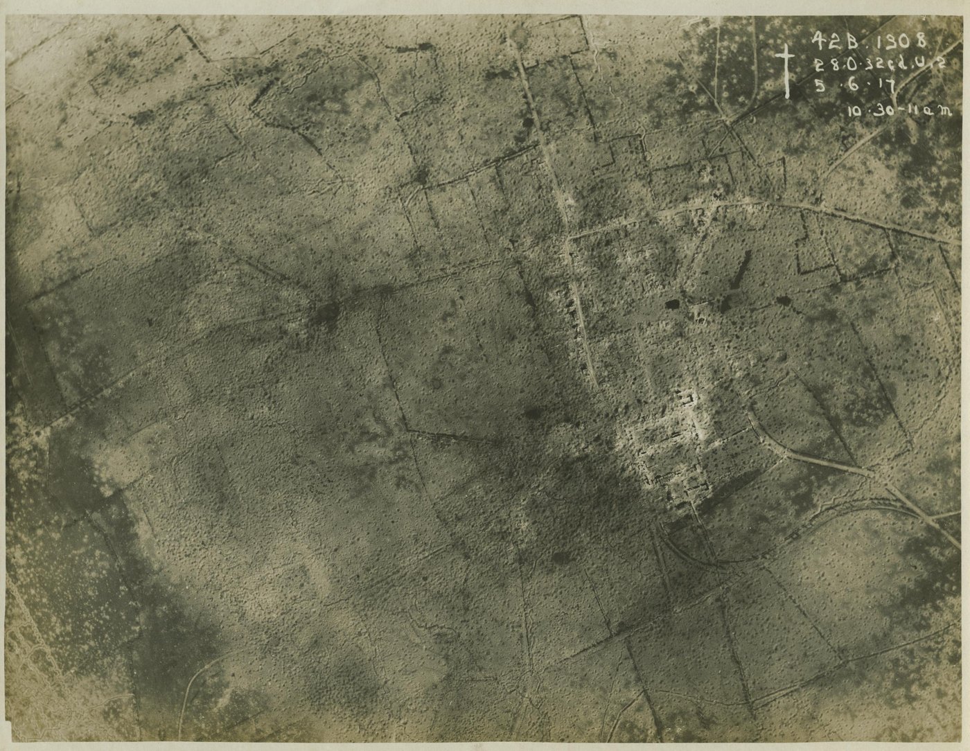 Sepia aerial photograph of farmland pitted with thousands of shell holes, crossed by zigzag trench lines and roads, with the pale ruins of a village at right and handwritten reference numbers and the date 5.6.17 in the top corner