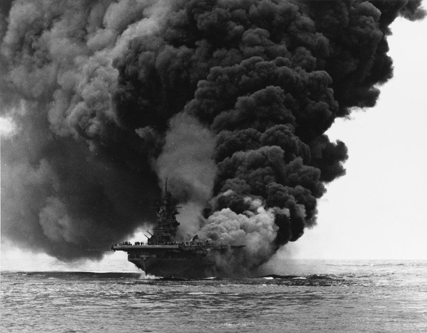 Huge column of black smoke rising from an aircraft carrier at sea