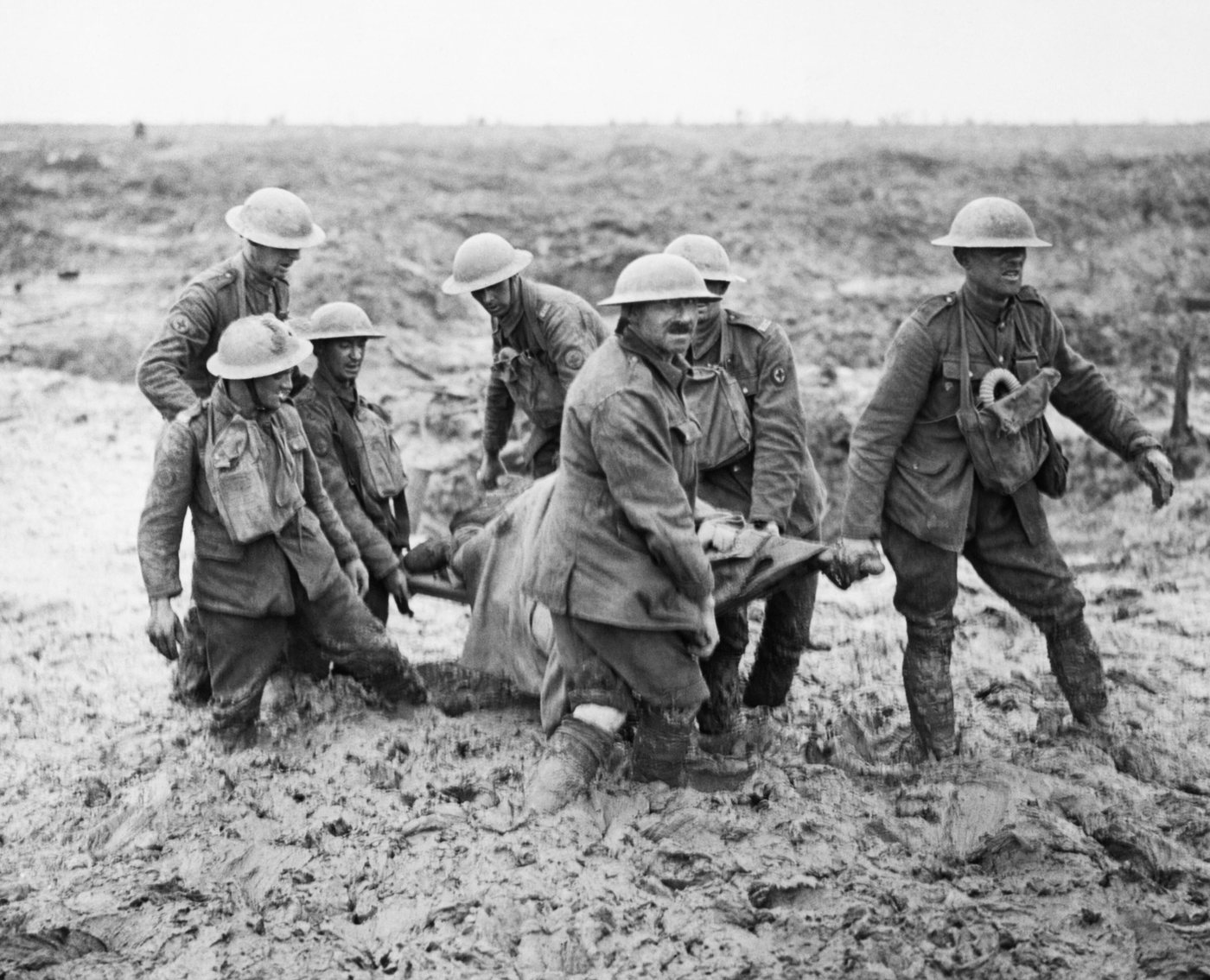 Six British soldiers carrying a wounded man on a stretcher through deep mud