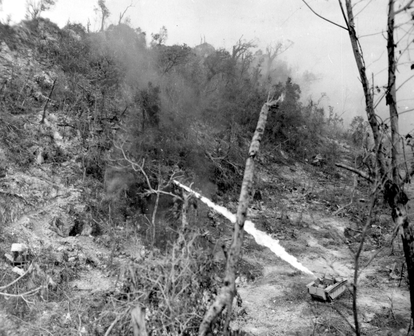 A tracked vehicle shooting a long jet of flame up a scrub covered slope