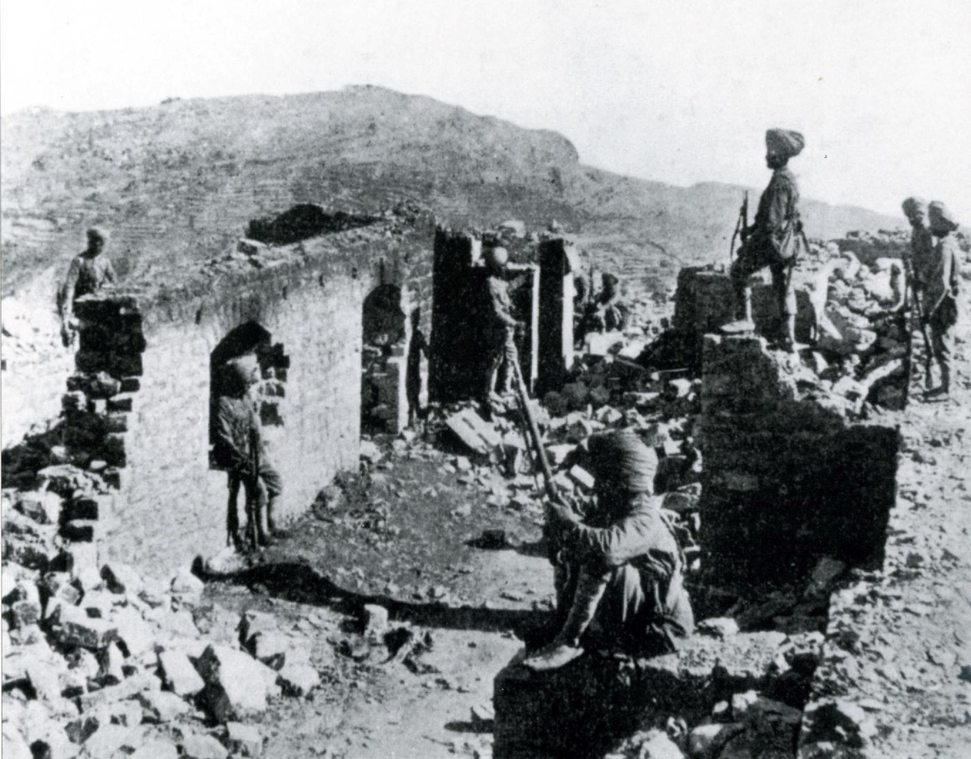 Black and white photograph of shattered stone walls on a rocky ridge with soldiers standing among the ruins