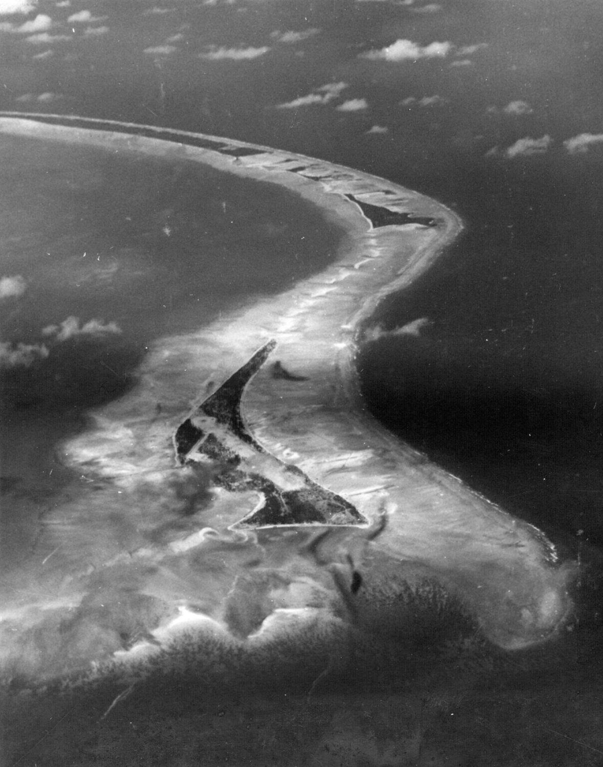 Aerial photograph of a narrow curving atoll with the small island of Betio and its airstrip