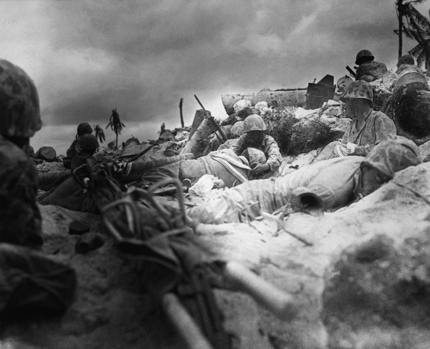 Photograph of Marines lying behind a low sea wall on a beach