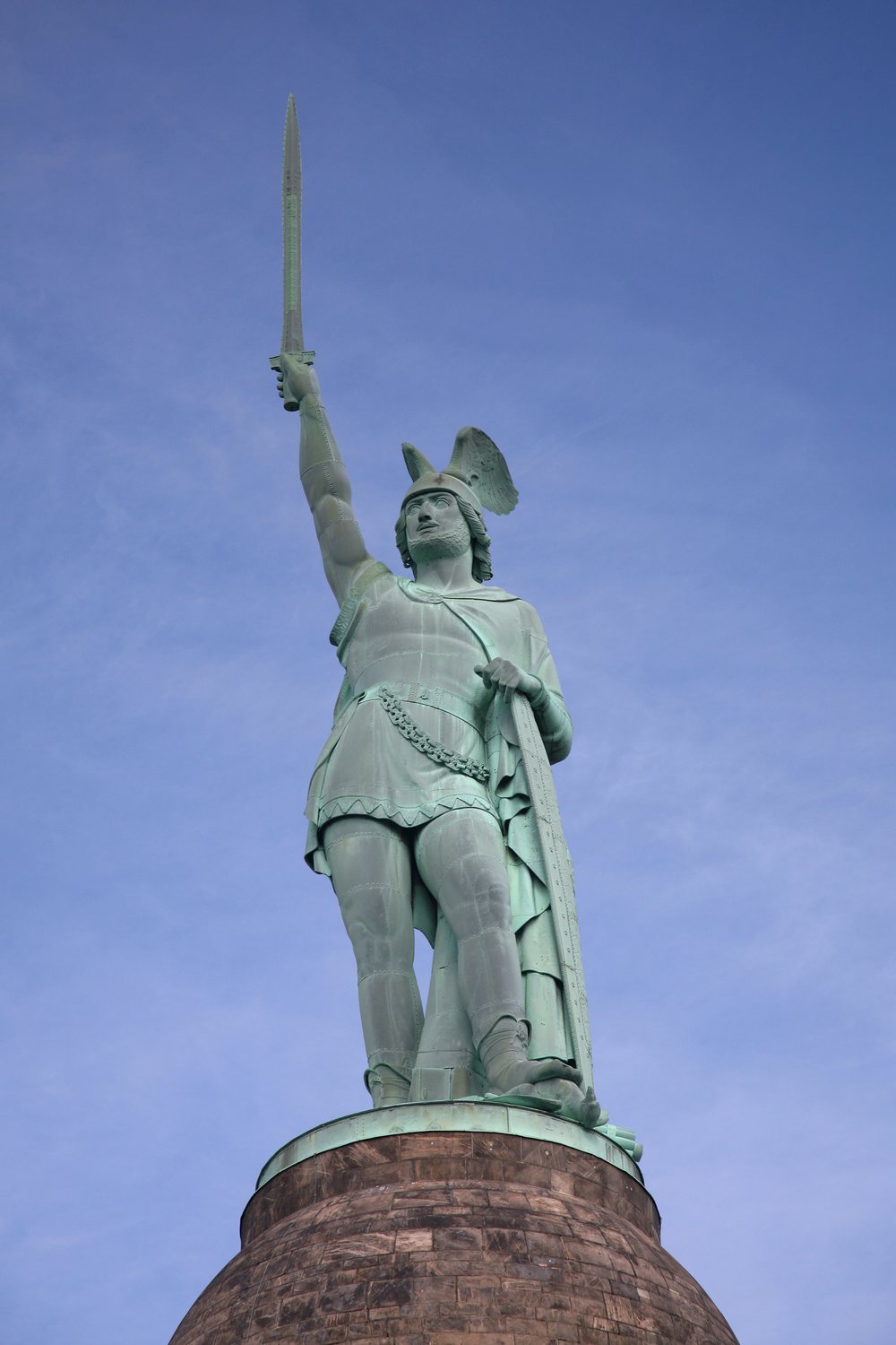 Copper statue of Arminius raising a sword on top of a stone pedestal