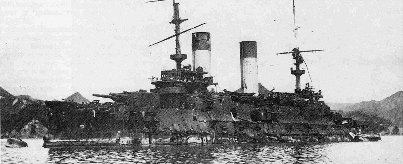 Black and white photograph of a battered Russian battleship lying low in a harbour