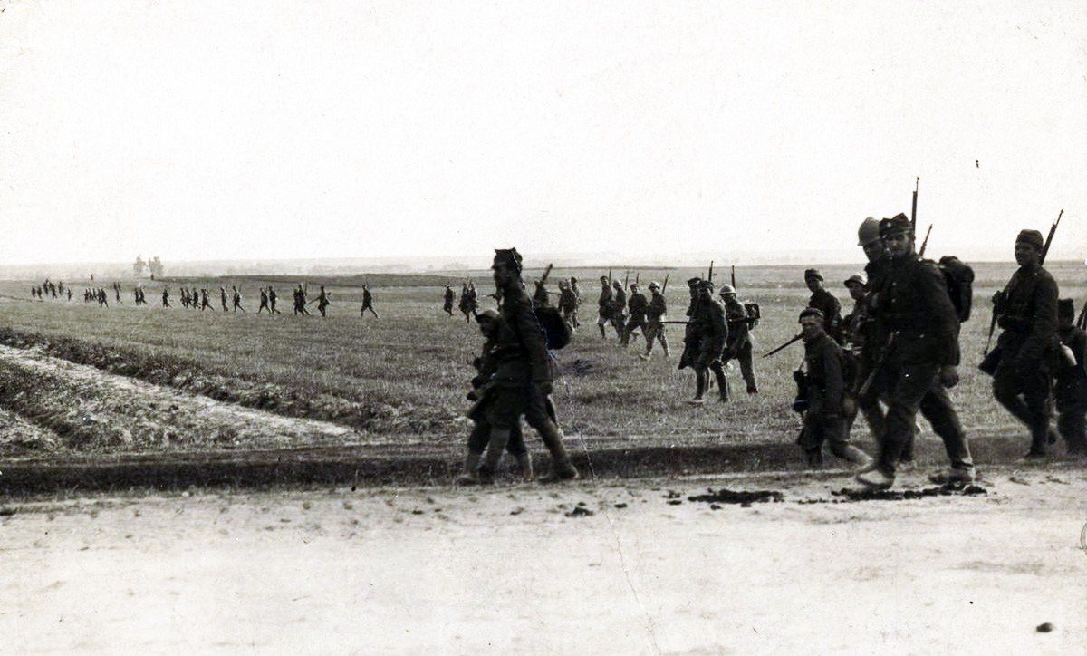 Black and white photograph of soldiers advancing in a line across flat farmland