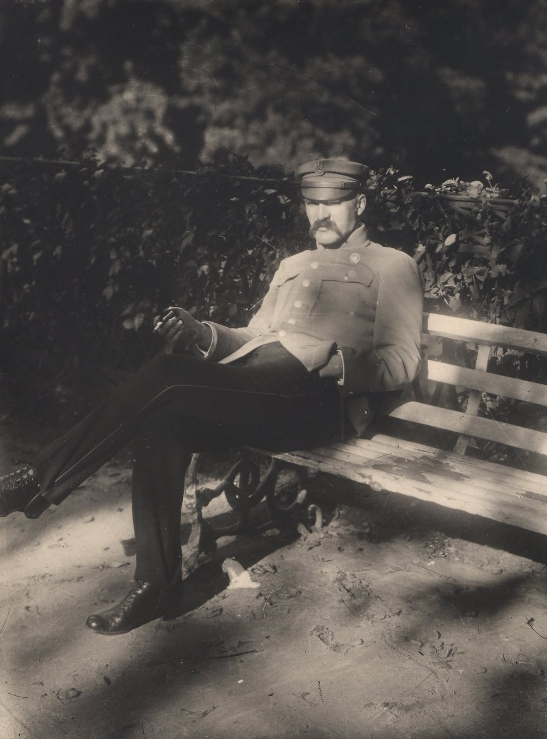 Sepia photograph of a moustached man in a military tunic seated on a park bench