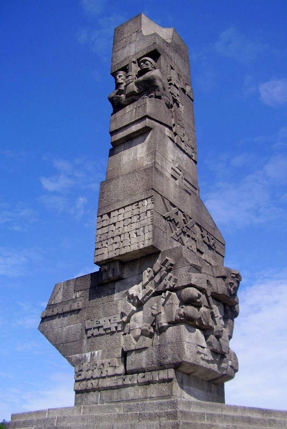 Tall granite monument with carved soldier figures standing against a blue sky