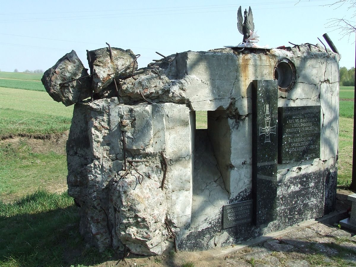 Ruined concrete bunker with memorial plaques and an eagle on top in a field
