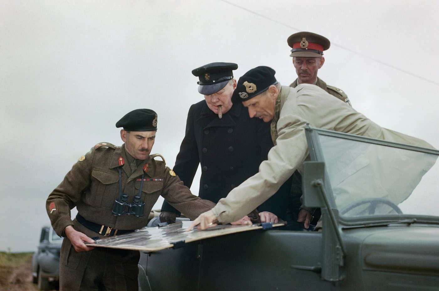 Montgomery pointing at a map held up for Churchill by officers outdoors