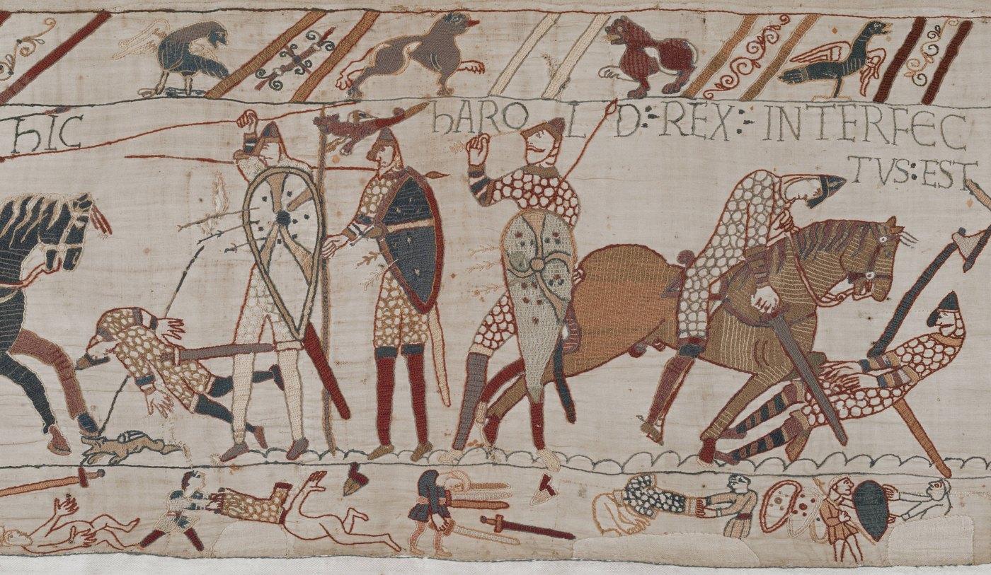 Section of the Bayeux Tapestry: mounted Norman knights cut down English foot soldiers, a figure pulls at an arrow near his eye, and the Latin words Harold Rex interfectus est above.