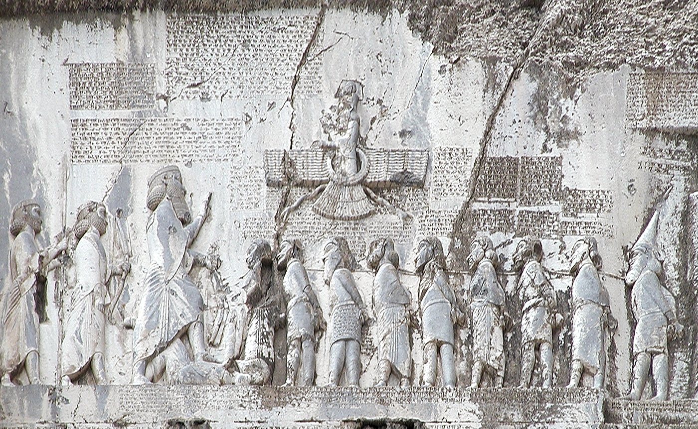 Rock relief of a king facing a line of bound captives beneath a winged symbol