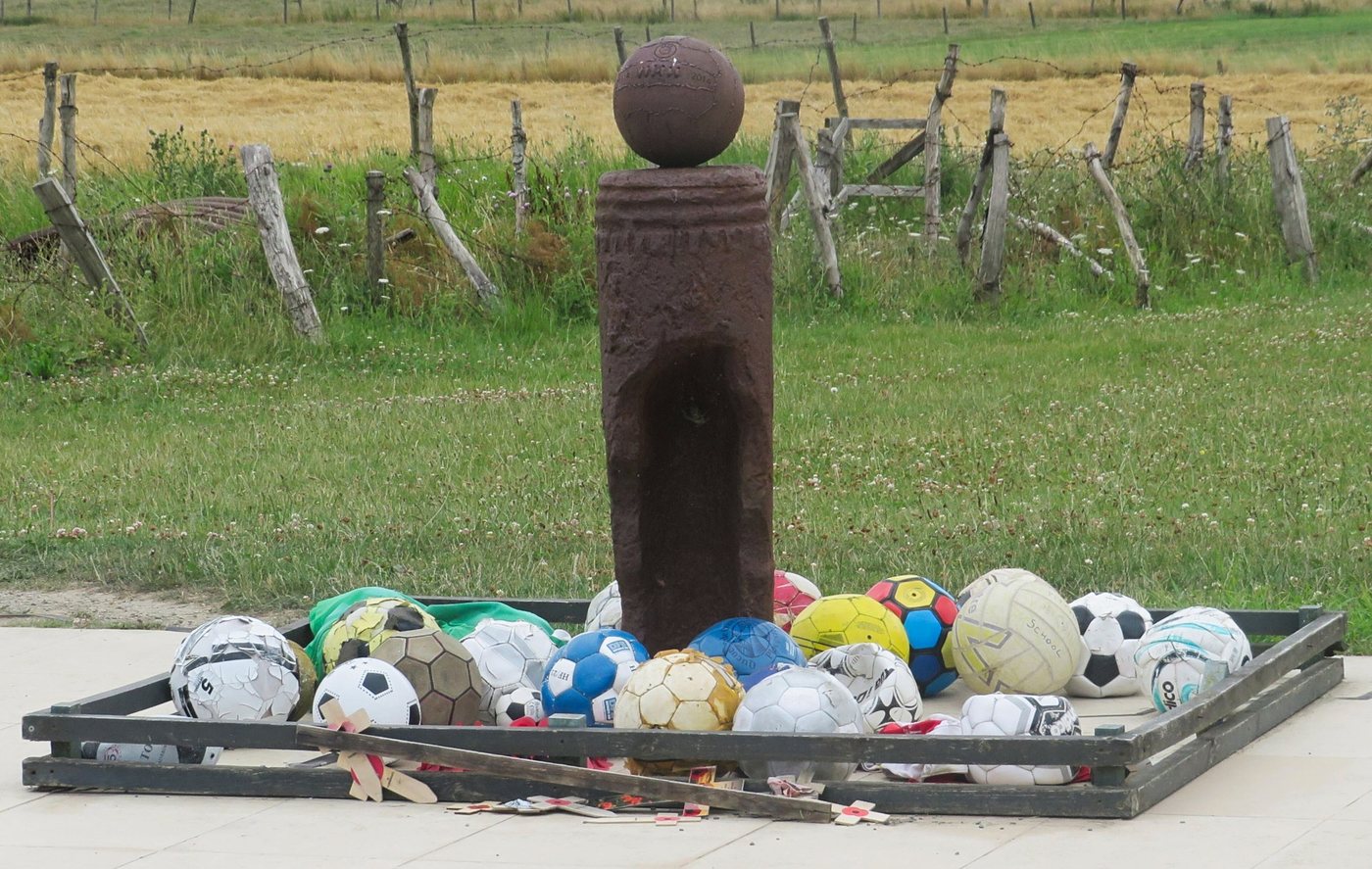 Memorial in a Belgian field made of a large artillery shell case with a football resting on top