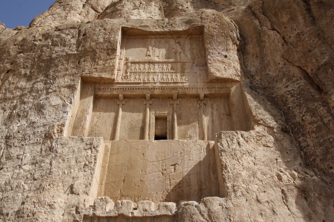 Photograph of a cross-shaped tomb facade carved into a sandstone cliff