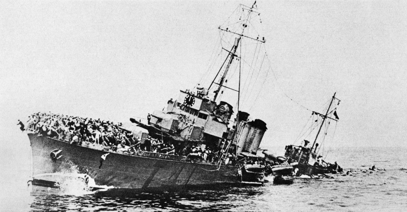 A listing warship packed with soldiers going down by the bow, with men in the water