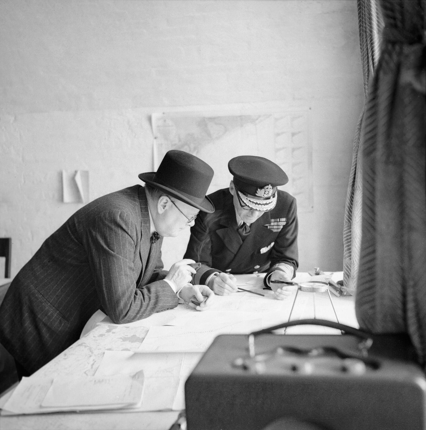 Churchill in a bowler hat and Admiral Ramsay in naval cap bending over maps on a table