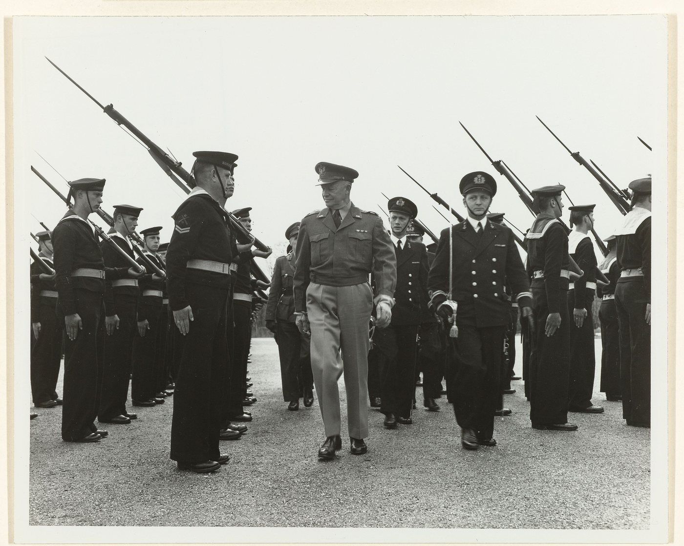 Black and white photograph of Eisenhower walking between ranks of sailors holding rifles with fixed bayonets